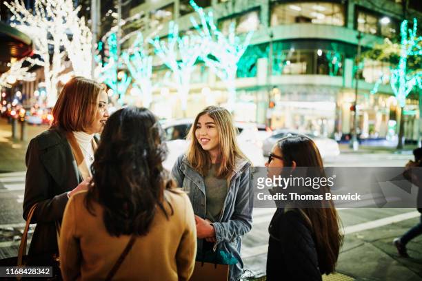 mothers and daughters in discussion on street corner while holiday shopping on winter evening - korean mexican woman stock pictures, royalty-free photos & images