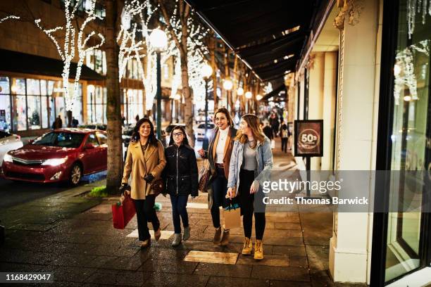 Two mature women and teenage daughters walking on sidewalk while shopping during holidays