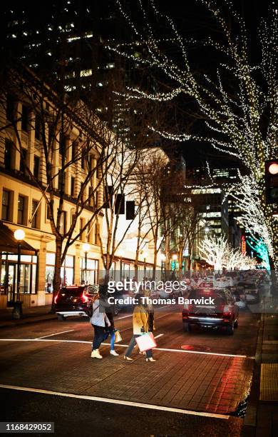two mature women and teenage daughters crossing street while holiday shopping on winter evening - korean mexican woman stock pictures, royalty-free photos & images