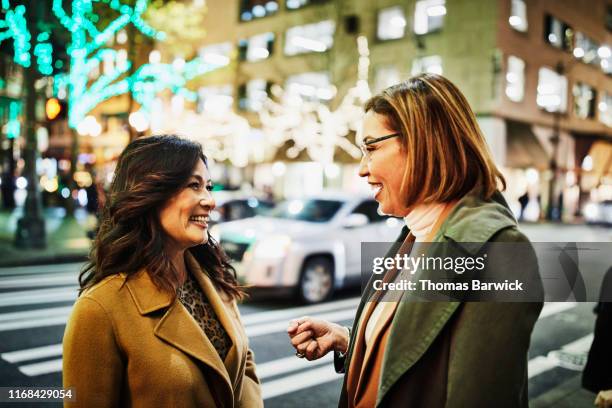 smiling mature women in discussion on street corner while holiday shopping on winter evening - camel active fotografías e imágenes de stock