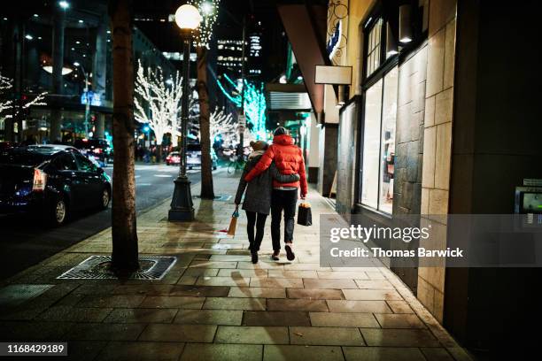 rear view of embracing couple walking down street while holiday shopping - auto von hinten winter stock-fotos und bilder