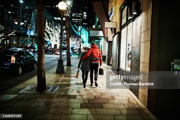 rear view of embracing couple walking down street while holiday shopping - sidewalk christmas lights stock pictures, royalty-free photos & images
