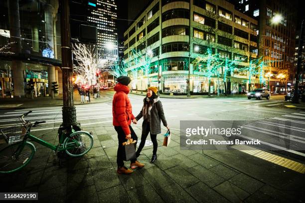 Smiling couple holding hands on street corner while holiday shopping on winter evening