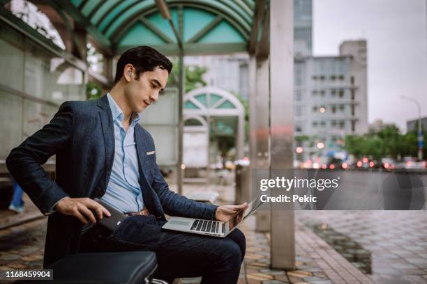 handsome man typing an e-mail while waiting for a bus - hearing loss at work stock pictures, royalty-free photos & images