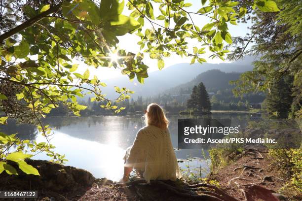 woman relaxes on mountain lakeshore at sunrise - evasión fotografías e imágenes de stock