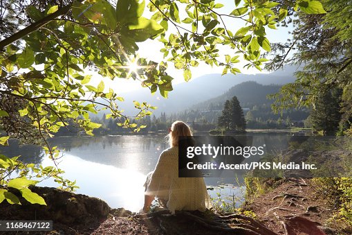 Woman relaxes on mountain lakeshore at sunrise Woman relaxes on mountain lakeshore at sunrise