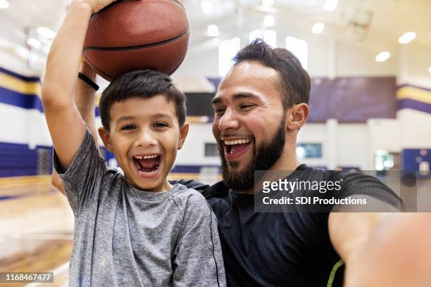 vater macht selfie, während sohn hält einen basketball auf dem kopf - basketball sport stock-fotos und bilder