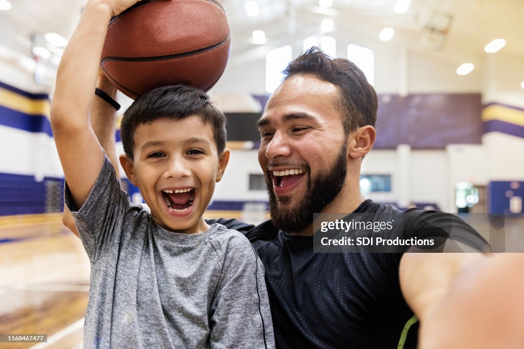 Padre se hace selfie mientras su hijo sostiene una pelota de baloncesto en la cabeza