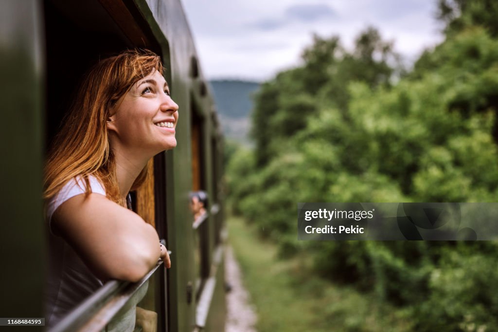 Joven mujer sonriente de pie por la ventana del tren mientras viaja