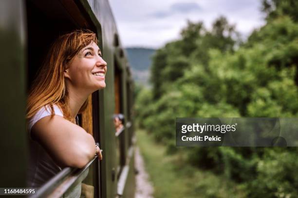 joven mujer sonriente de pie por la ventana del tren mientras viaja - journey fotografías e imágenes de stock