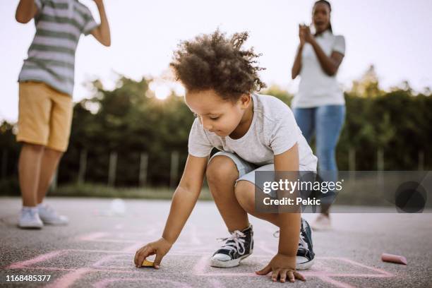 african girl drawing hopscotch on asphalt with friends - hopscotch stock pictures, royalty-free photos & images