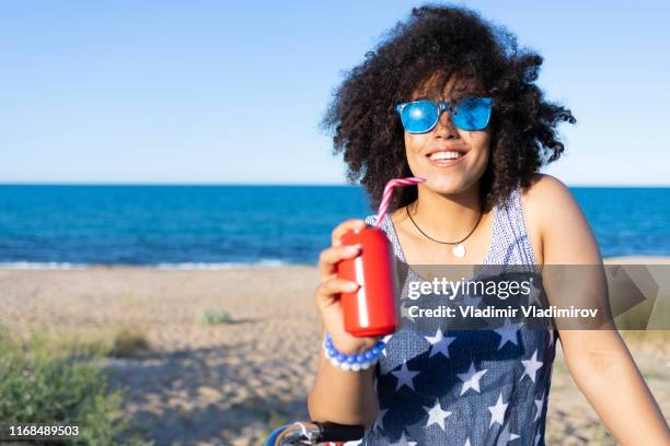 zorgeloze afrikaanse vrouw drinken rode kan op het strand - african girl drinking water stockfoto's en -beelden