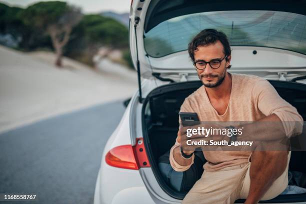 joven sentado en el maletero del coche - coche carretera fotografías e imágenes de stock