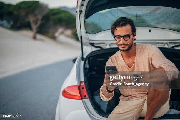 young man sitting on car trunk - car imagens e fotografias de stock