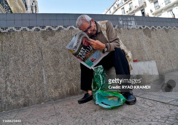 Man reads an Algerian French-language newspaper, with its cover dominated by the announced Algerian presidential election date, as he sits a along...
