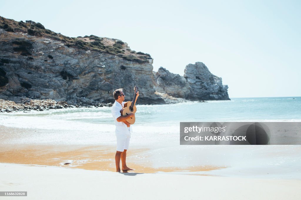 Man with white shirt playing guitar at beach