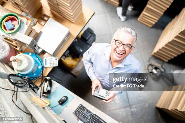 top view of a senior man in a storage room holding calculator looking at camera - calculator top view stock pictures, royalty-free photos & images