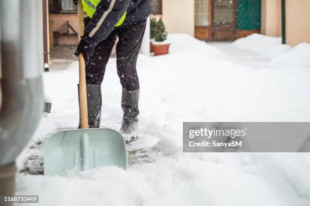 man with snow shovel cleans sidewalk - shovel stock pictures, royalty-free photos & images