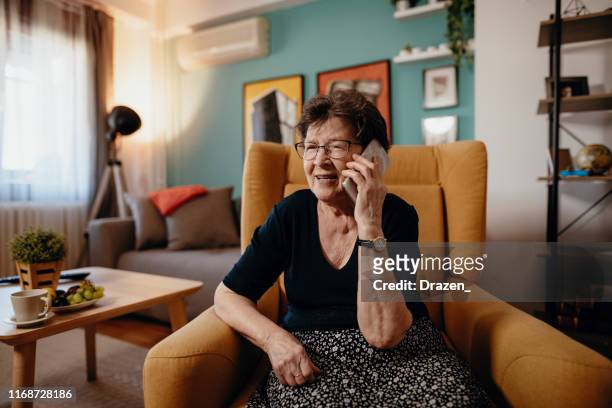 retrato de mujer senior en casa usando teléfono móvil y tecnologías - old phone fotografías e imágenes de stock
