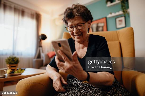 portret van senior vrouw thuis met behulp van mobiele telefoon en technologieën - oost europese etniciteit stockfoto's en -beelden