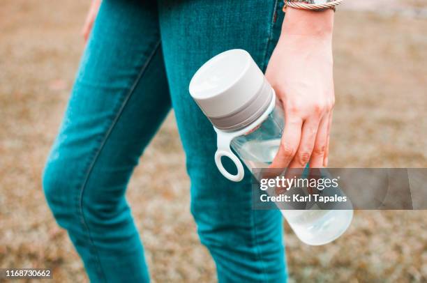 a young woman is holding a reusable water bottle container outdoors - bottle water fotografías e imágenes de stock