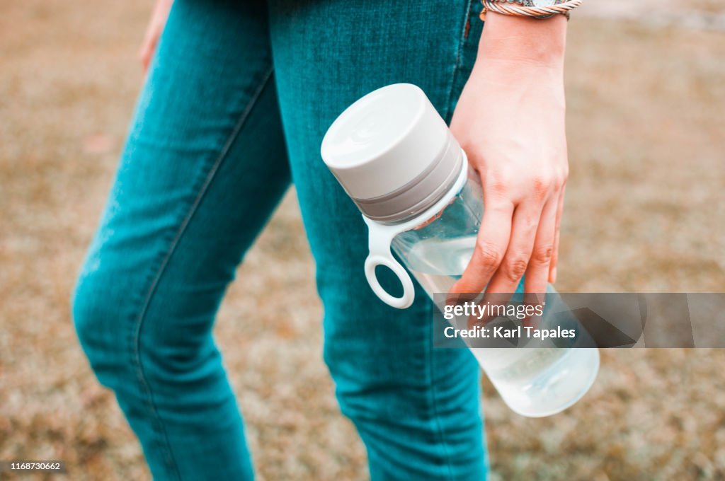 A young woman is holding a reusable water bottle container outdoors