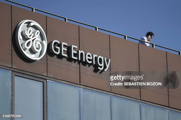 Man phones atop the building of US giant General Electric past the logo of the company in Belfort, eastern France, on September 17, 2019. - About a...