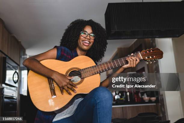 ragazza adolescente sorridente che tiene in mano una chitarra acustica a casa - plucking an instrument foto e immagini stock