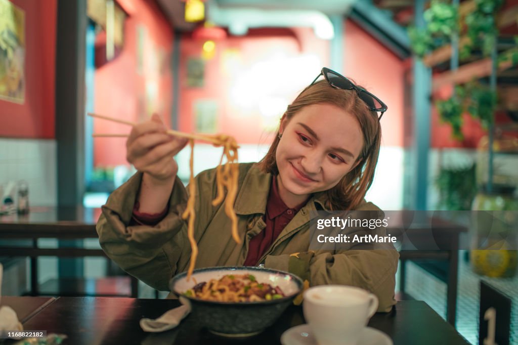 Young girl eating Chinese food in a restaurant in autumn