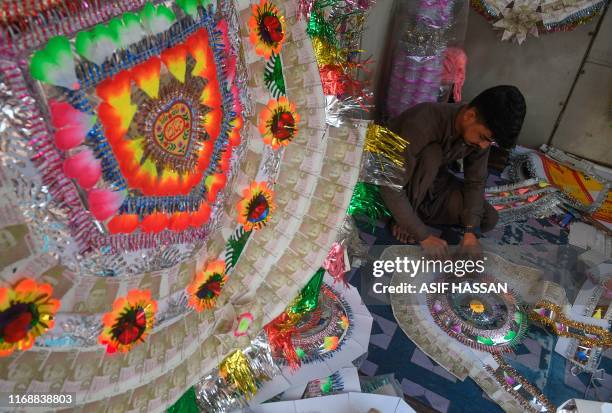 Vendor makes garlands with banknotes at a roadside shop in Karachi on September 17, 2019. - Garlands made with bank notes are widely used during...