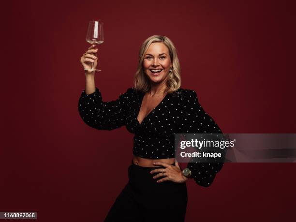 woman cheering with glass of wine in studio against red - holding aloft stock pictures, royalty-free photos & images