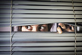 Brown-eyed girl peeps fearfully through venetian blinds