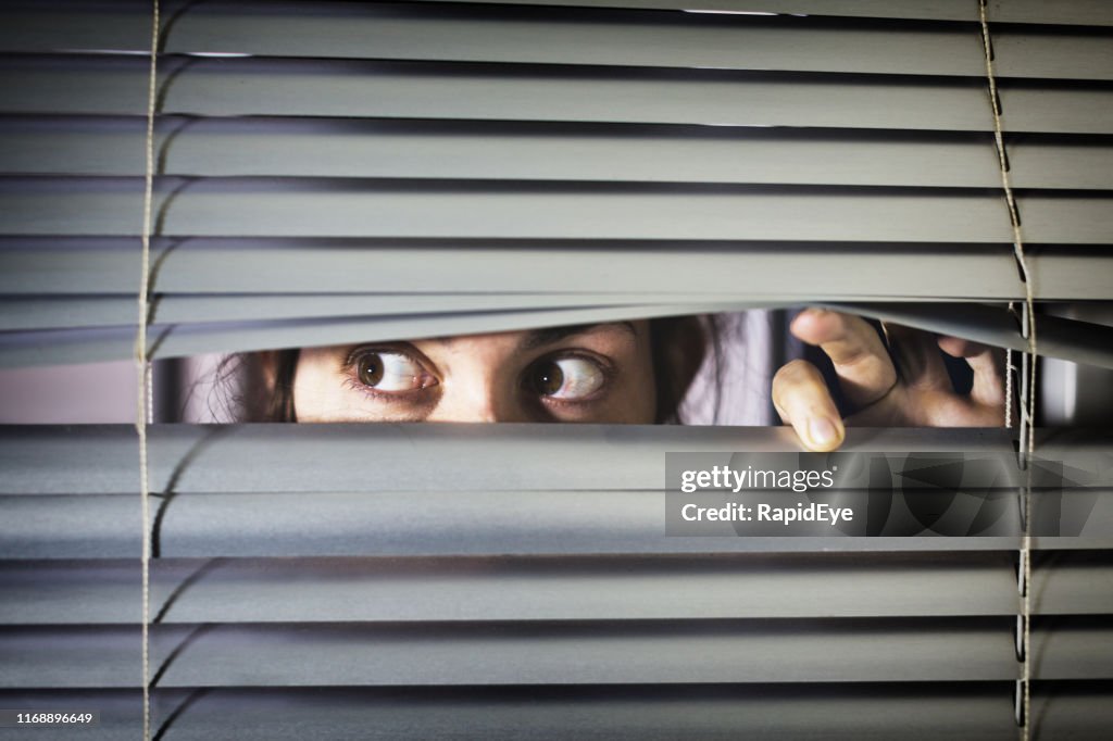 Brown-eyed girl peeps fearfully through venetian blinds