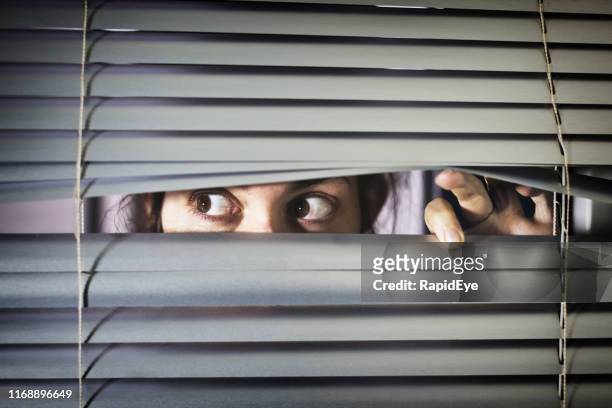 brown-eyed girl peeps fearfully through venetian blinds - peeking through stock pictures, royalty-free photos & images