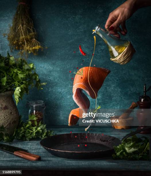 flying salmon fillet with herbs, spices and female hand with pouring olives oil - levitation stock-fotos und bilder