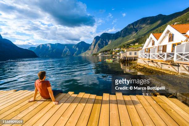 man sitting on wooden pier admiring a norwegian fjord, western norway - cultura norueguesa imagens e fotografias de stock