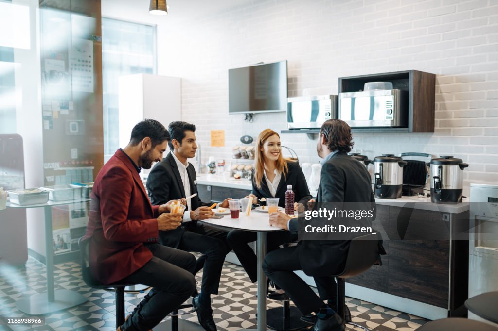 Millennial Latin coworkers taking a break at work, eating snack and chatting.
