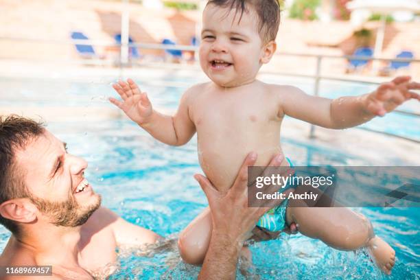glücklicher kleiner junge mit seinem vater im schwimmbad - babyschwimmen stock-fotos und bilder