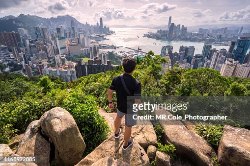 Asian man traveler is visiting at Braemar hill peak,tourist looking to Hong Kong City view and Victoria harbor