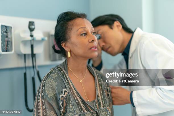 mature adult woman has ears checked by doctor at routine medical appointment - hearing aids stock pictures, royalty-free photos & images