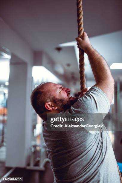 overweight male giving his best to compete rope climbing exercise - toughness stock pictures, royalty-free photos & images