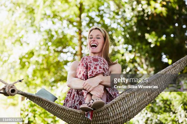 portrait of a content middle aged happy woman sitting in a hammock - garden summer enjoy stock-fotos und bilder