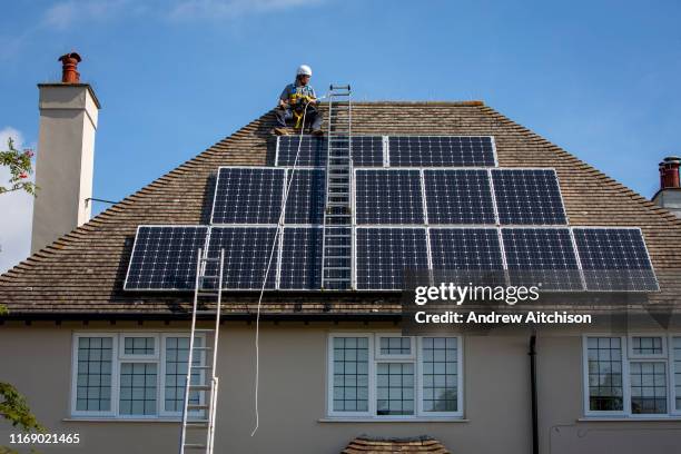 Maintenance person uses a ladder and harnesses to install equipment around a Solar panel array on the roof of a house to stop birds nesting...