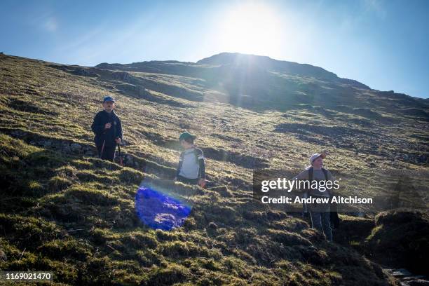 Three children stop and have a break while walking up a steep path on Helvellyn Mountain, Lake District, Cumbria, UK. Helvellyn is the third-highest...