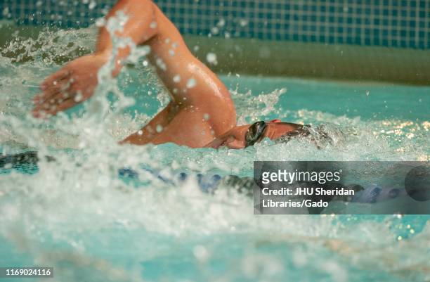 Obscured profile shot of a Johns Hopkins University Men's Swim team member, from the chest up, moving through the water while performing a...