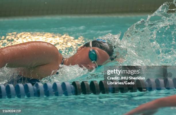 Obscured profile shot, from the chest up, of a Johns Hopkins University Men's Swim team member, moving through the water while performing a...