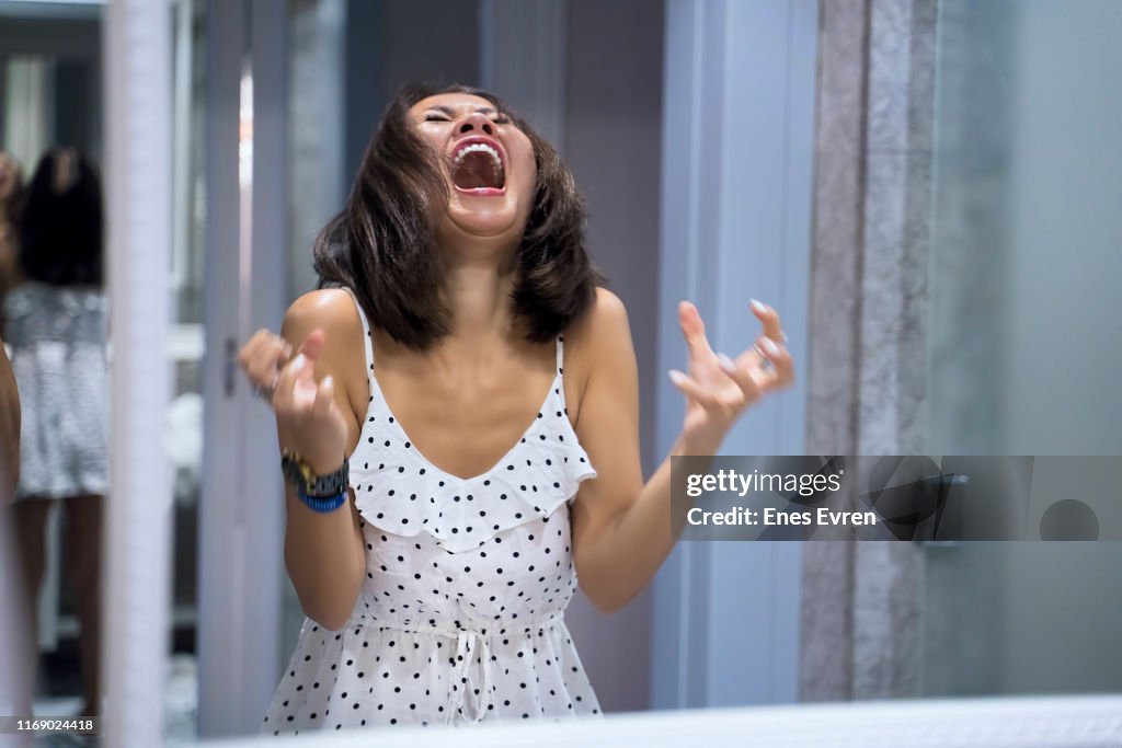 Angry woman shouting at mirror and crying