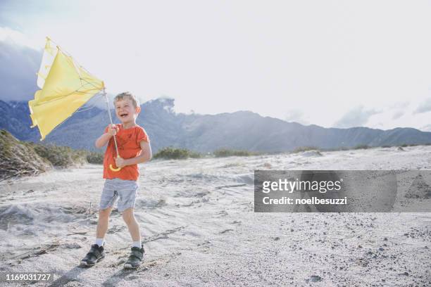 laughing boy standing in the desert holding a broken umbrella, palm springs, california, united states - broken umbrella stockfoto's en -beelden