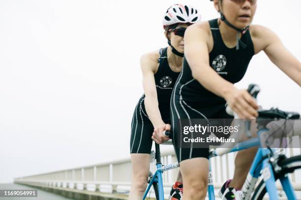 visually impaired female triathlete training together with her guide and coach on a tandem bicycle - tandem stock pictures, royalty-free photos & images