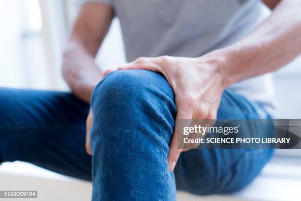 man holding his left knee in pain - schmerz stock-fotos und bilder